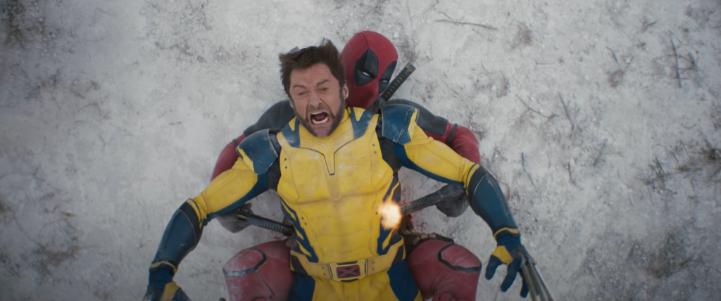 Deadpool e Wolverine deitados um em cima do outro na neve, enquanto o deadpool dispara dois tiros de arma no wolverine.